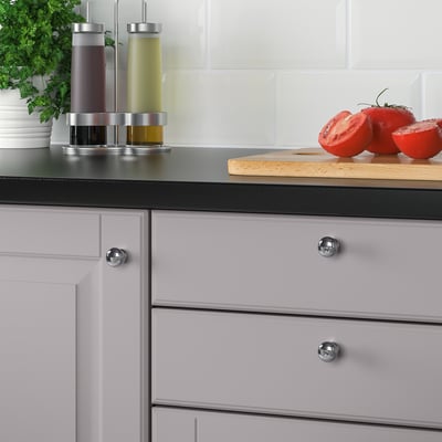 Modern kitchen cabinets with chrome knobs and a black countertop, featuring a cutting board with sliced tomatoes and condiments.