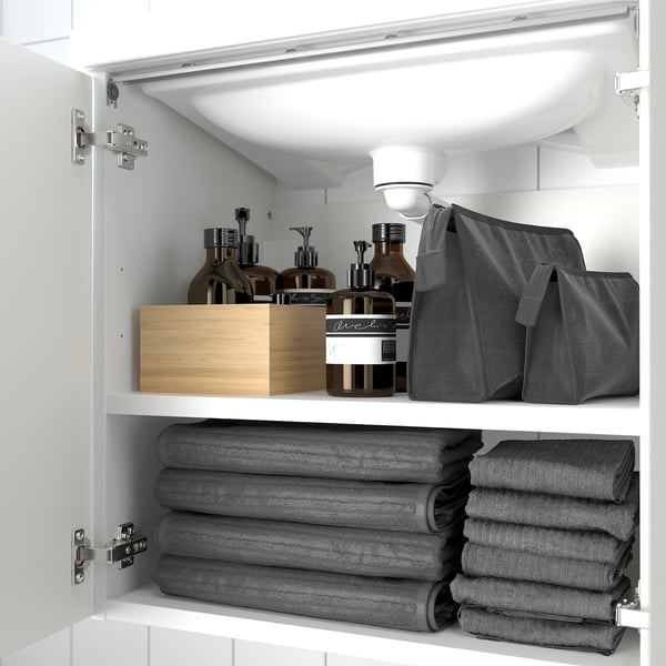 Cabinet with folded grey towels and toiletries on shelves.