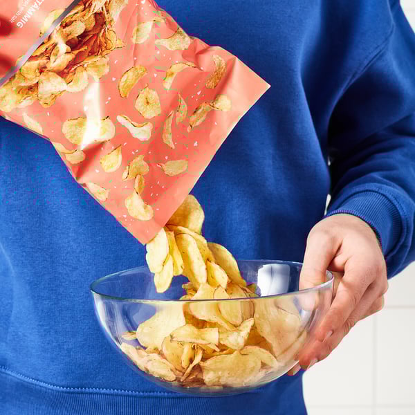 Person pouring rustic potato crisps from red pack into clear bowl.
