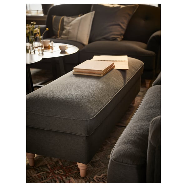 Living room with ESSEBODA grey fabric bench, cushioned seat, wooden legs. Books on top, coffee table with cups nearby, plush sofa.