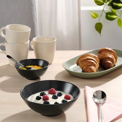 Breakfast table with FÄRGKLAR bowls, cups, croissants, yoghurt, berries, cereal, napkin, and spoon.