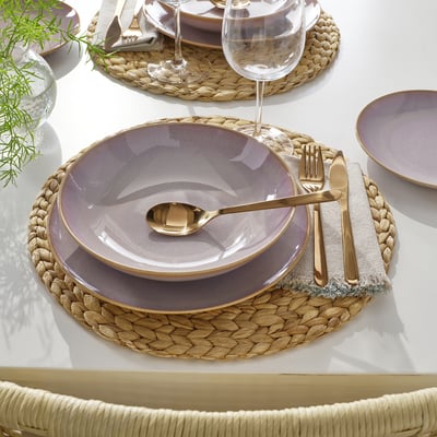 Elegant place setting with purple plates, gold cutlery, and woven placemat on a white table. Perfect for stylish meals.