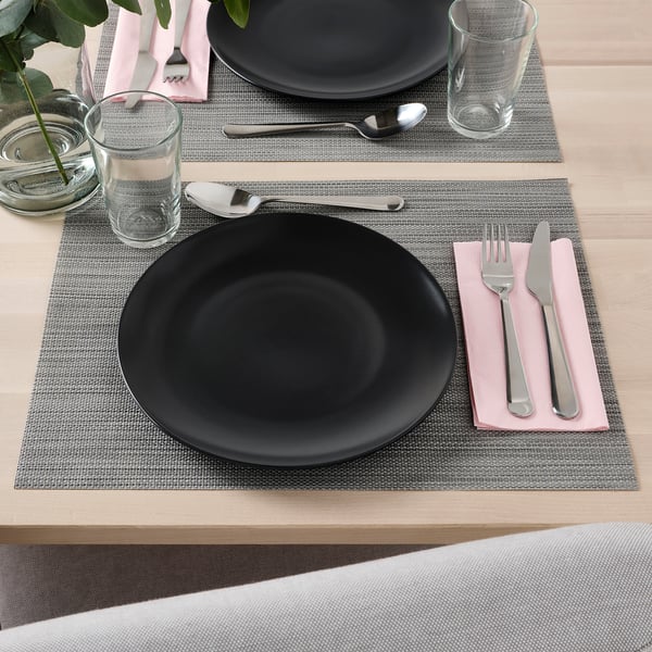 Table setting with FÄRGKLAR black plate, silverware, glass, and napkin.