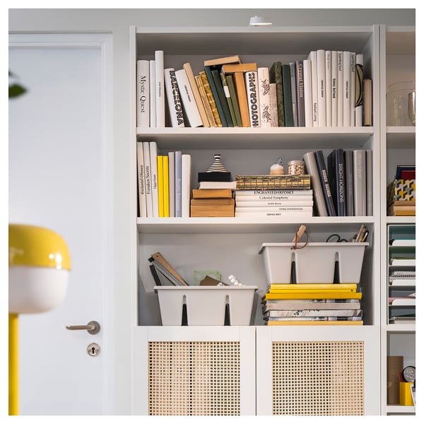 A white bookshelf with various books and items. Includes a yellow lamp and mesh storage baskets.