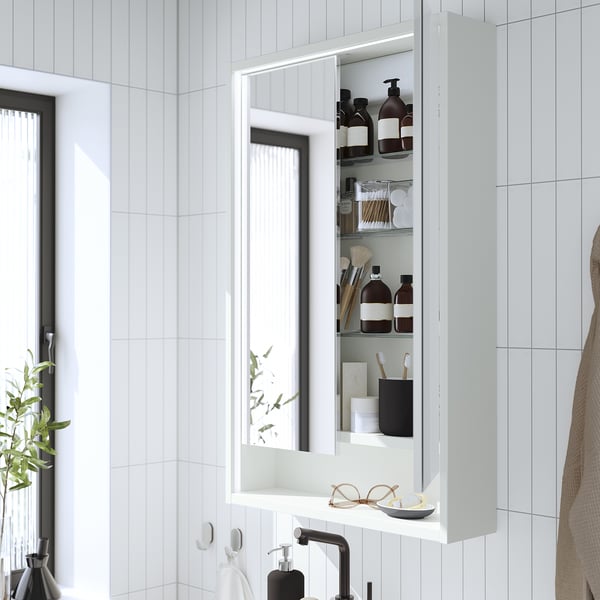 White mirrored bathroom cabinet with integrated lighting, revealing shelves of toiletries and bathroom items.