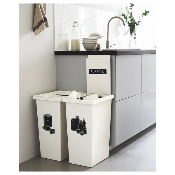 Modern kitchen scene with two white FILUR recycling bins labelled plastic and glass, positioned under a counter with a sink and a potted plant.