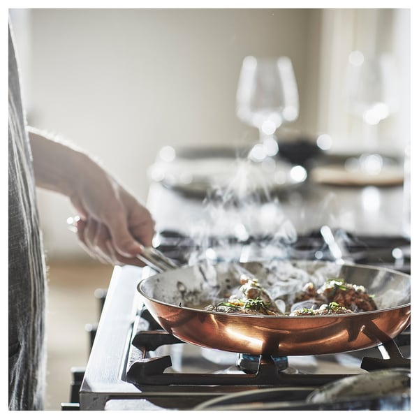 Copper FINMAT frying pan on stove, stainless handles, steam rising.