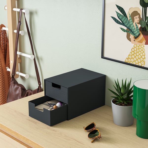 Black mini chest with open drawer on wooden table, glasses, plant, bag hooks, artwork.