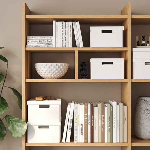 Wooden bookshelf with white storage boxes, books, and decorative items.