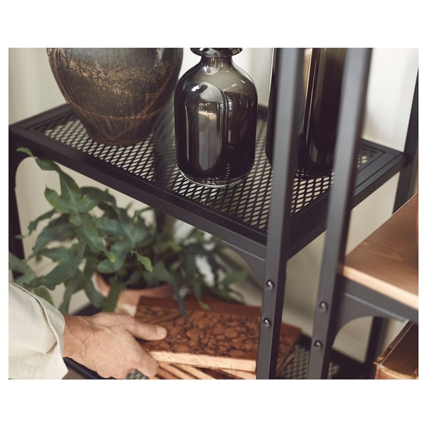 Black metal shelf with wooden panels holds decorative vases and a plant.