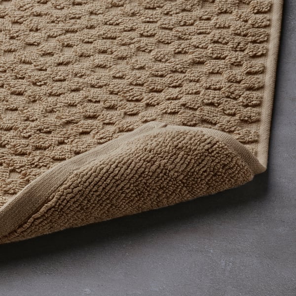 Beige bath mat with textured cotton surface, high absorption, folded edge.