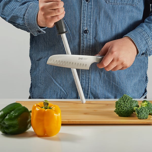 A person sharpens a knife using an IKEA FLAKSA sharpener with vegetables nearby.