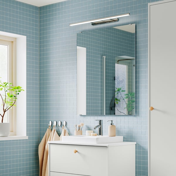 Modern bathroom with blue tiles, chrome FLASKPOST led light, mirror, and white sink. Glare-free, adjustable light for tasks.