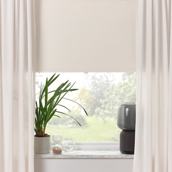 Window with beige roller blind and potted plant. Clean, bright room with white curtains.