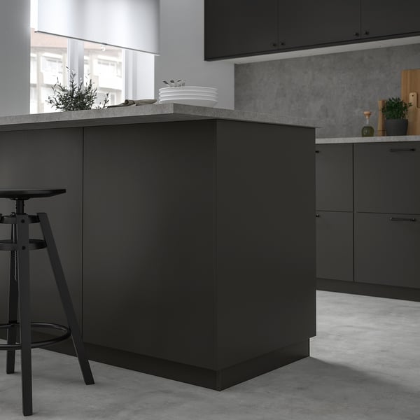 Modern kitchen with large black FÖRBÄTTRA island, sleek countertop, and single stool, contrasting with light floor and walls.
