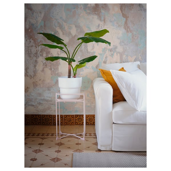 A cosy room with a white cushioned chair, a small potted plant on a pink stand against a textured wall.