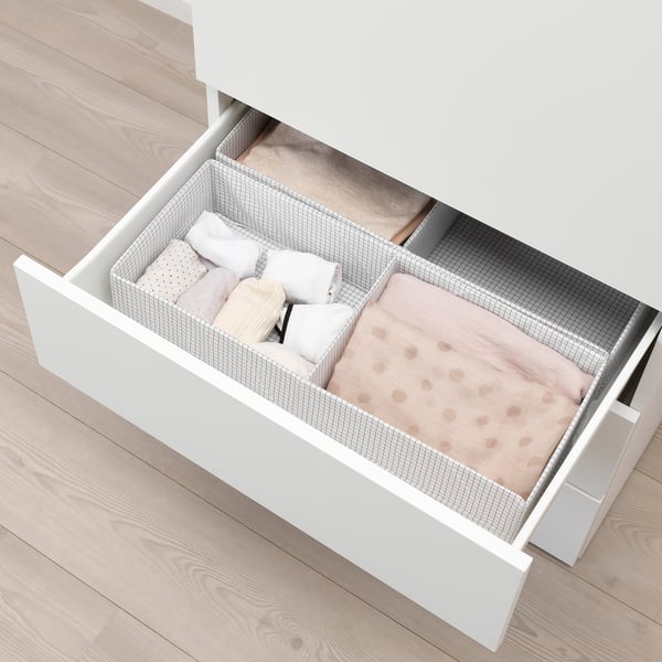 Open white cabinet drawer displaying neatly folded light pink blanket and pillows on wooden floor.