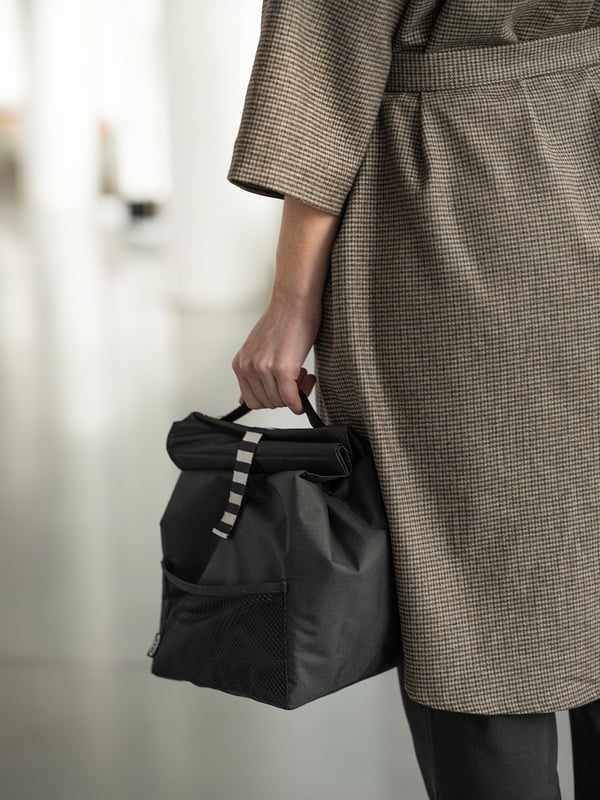 Person holding black, round-handled FRAMTUNG bag, chequered grey coat.