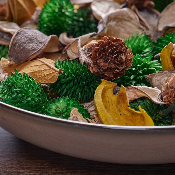 Vibrant potpourri mix: green needles, brown pinecone, dried leaves, and orange peel. Evokes warm, woodsy scent.