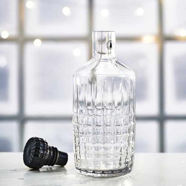 Clear, faceted glass carafe with black stopper, elegant design, sits on a surface.