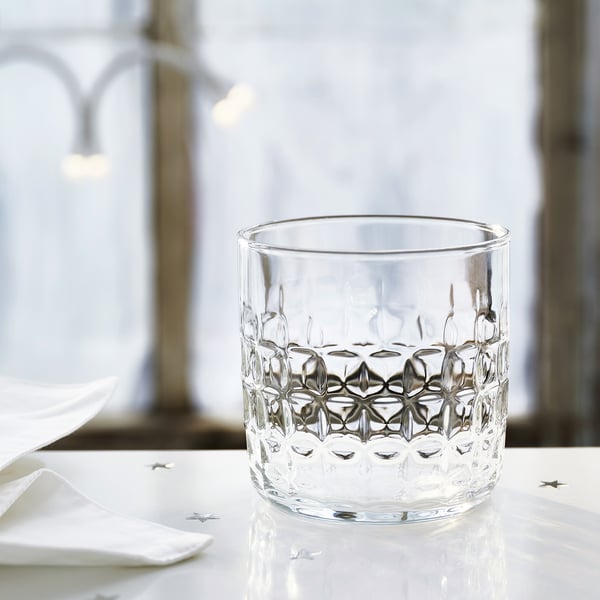 Glass cup with raised geometric patterns on white table, festive napkins, and star decorations.