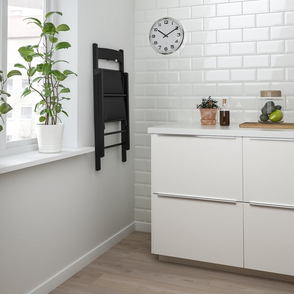 A modern kitchen with white cabinets, a clock, and a folding chair leaning against the wall.