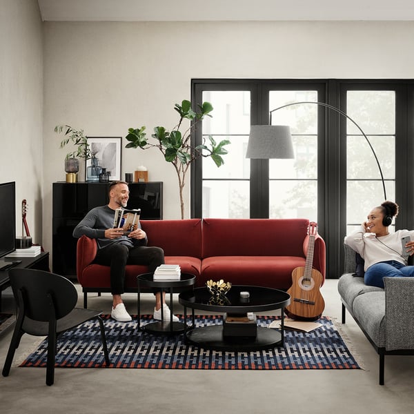 Cosy living room: red and grey couches, black side table, guitar, plants, large window.