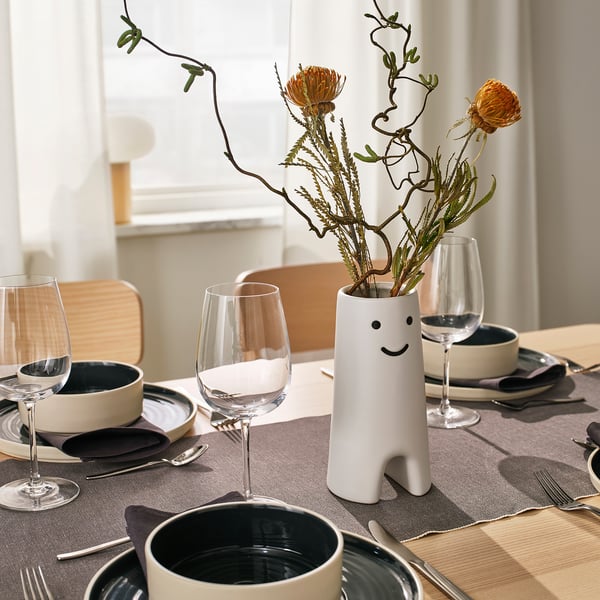 Decor: smiling flower vase with orange flowers and glasses on table.