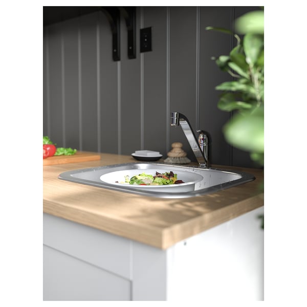 Modern kitchen sink in stainless steel, installed in wood countertop, with a plate of salad.