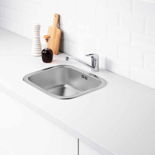 Stainless steel kitchen sink with tap on white countertop.