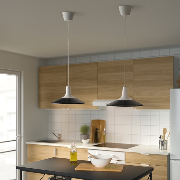 Modern black pendant lamps illuminate kitchen island, highlighting bowl and cutting board.
