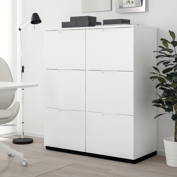 White GALANT storage unit with drawers, tall with modern design, beside desk, chair, and plant.