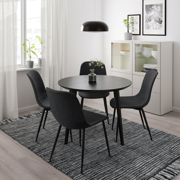 Modern dining setup with 4 black chairs, circular table, pendant light, and a rug.