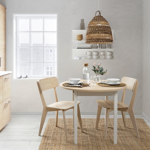 Modern kitchen with extendable table, chairs, rug, and lamp. Table set with dishes, glasses, and flowers.