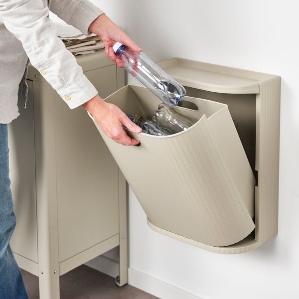 Person recycling plastic bottle into beige GÅRDSBUTIK wall-mounted bin.