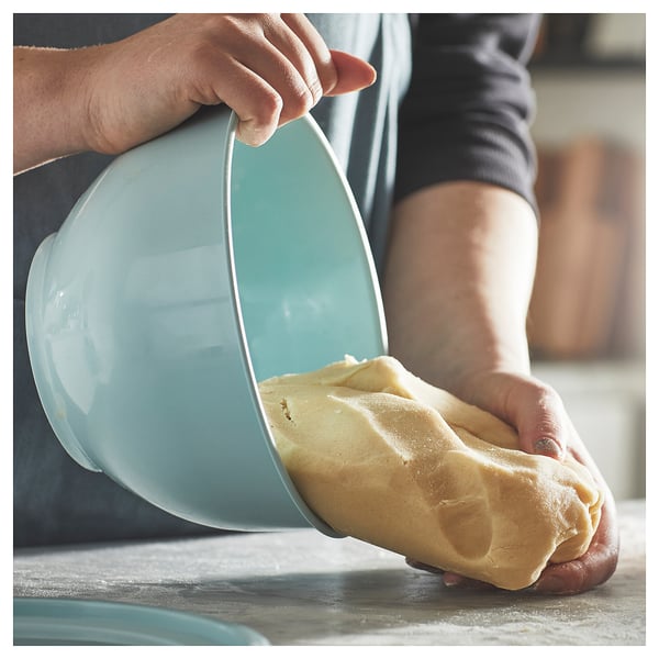 A person handles yellow dough beside a light blue plastic bowl.