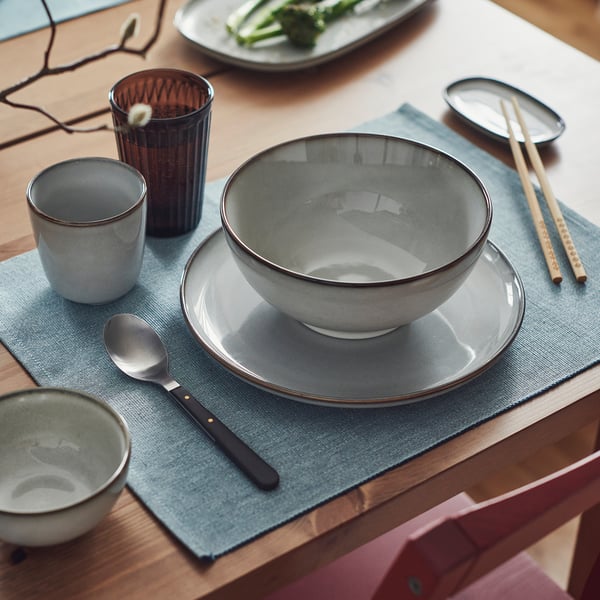 Grey GLADELIG bowl on table, sandy glaze, stoneware, with cups, chopsticks, and spoon.