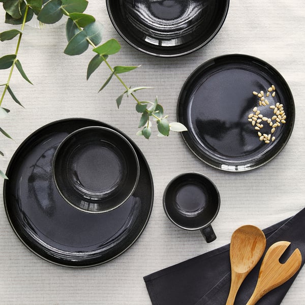 GLADELIG deep plate, dark grey, stoneware, round, crafted look, larger than smaller bowl, napkin, and spoons.