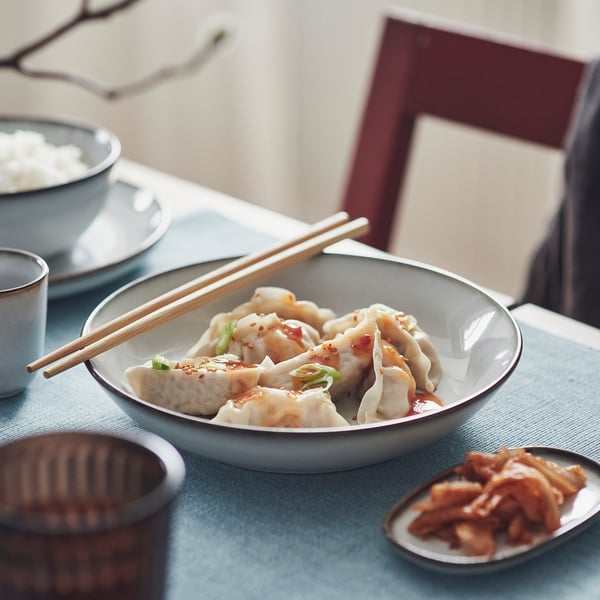 Blue bowl of dumplings with chopsticks and side dishes on a table.