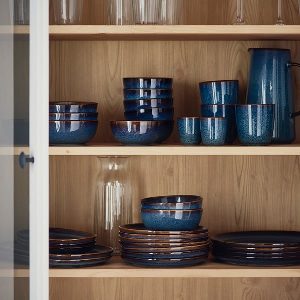 Wooden shelf with blue GLADELIG mugs, bowls, plates, and pitcher. Golden-brown details, stoneware.