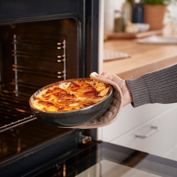 Person placing baked dish from oven, showcasing GLADELIGs oven-to-table functionality.