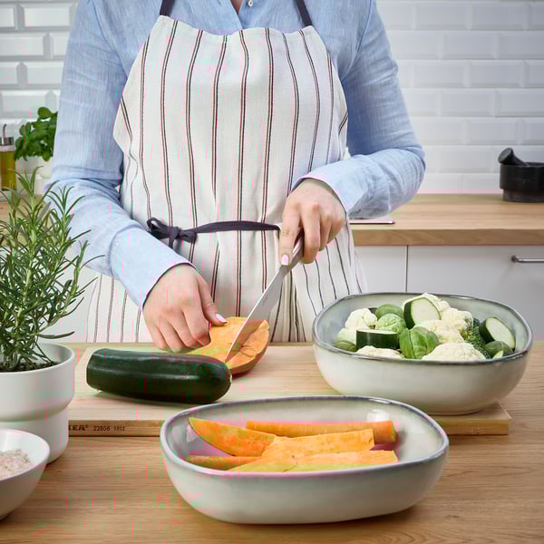 Person chopping vegetable beside bowls. Dish used for serving food directly from oven to table.