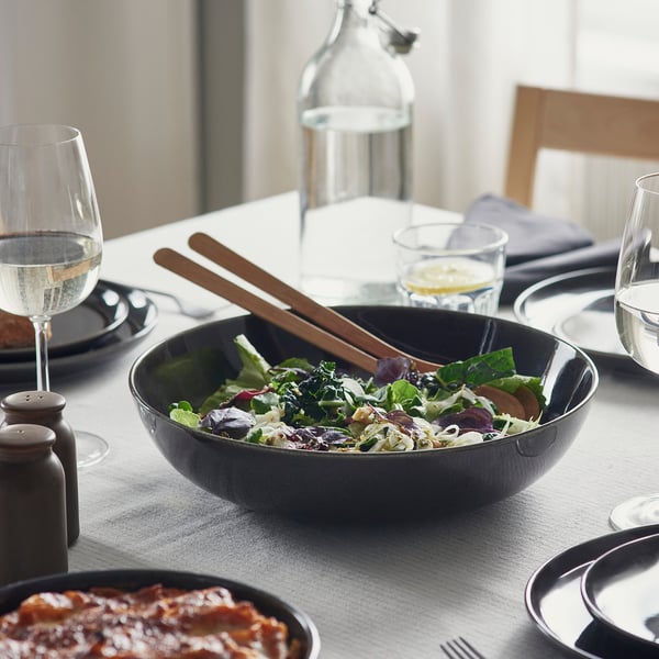Table set with grey GLADELIG bowl, wooden tongs, wine glasses, plates, and cutlery, featuring a mixed salad and lasagna.