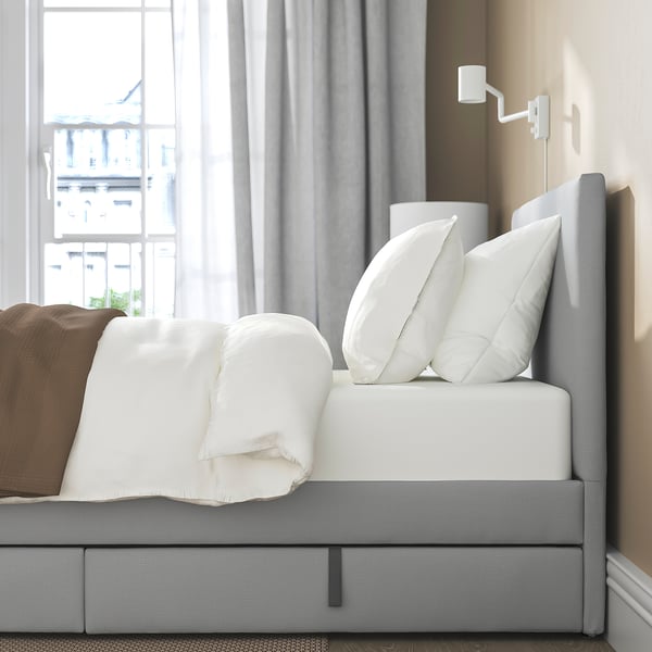 A modern bed frame with soft headboard and drawers for storage, positioned near a large window.