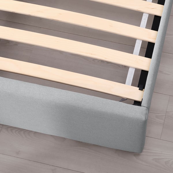 Upholstered bed frame with padded headboard, soft grey cover. Wood slats visible, showcasing storage space underneath.