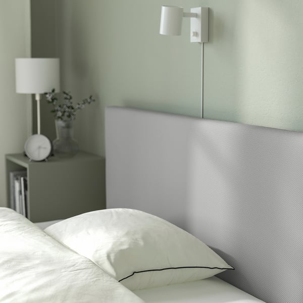 Modern minimalist bed with grey headboard, wall light, and bedside table with lamp and clock.