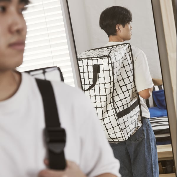 Two people demonstrate GÖRSNYGG bags: one as a backpack, adjustable straps; another by handles, versatile use.