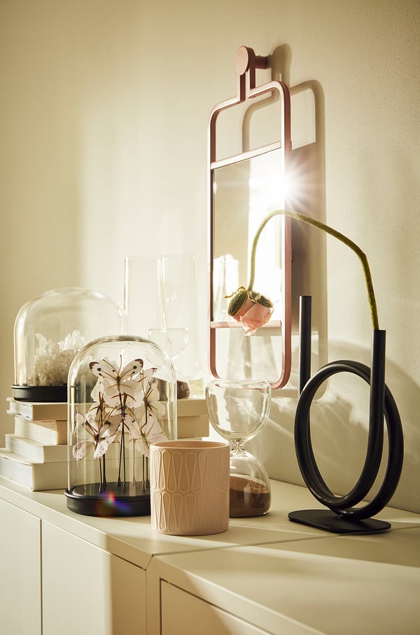 Shelf with GRANVÅG mirror, black sculpture, dried flowers, candle holder, books, vases, natural light.