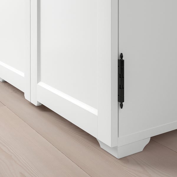 Modern white cabinet with sleek black handles positioned on a light wood floor, emphasising quality and design.