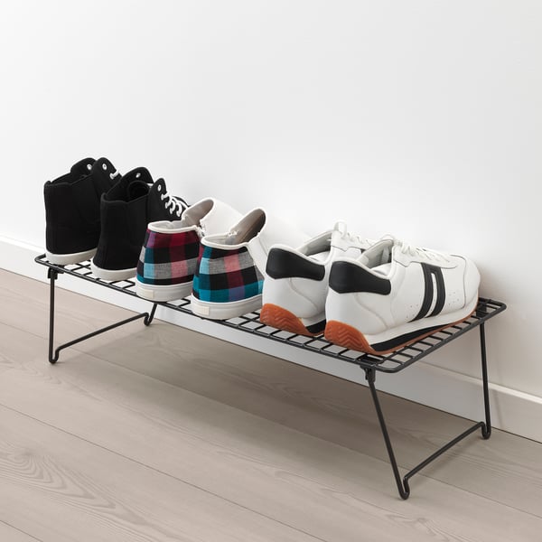 Black wire shoe rack against a wall, holding three pairs of trainers.